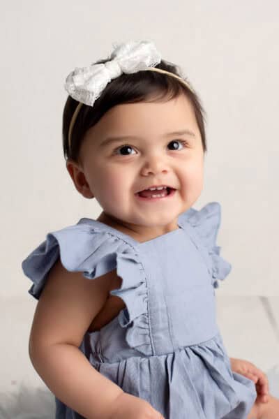 A baby girl wearing a blue dress and a white bow.