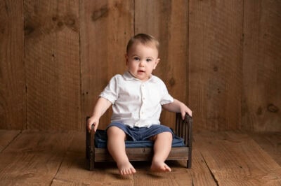 A baby boy sitting in a wooden chair.