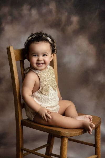 A baby girl sitting on a wooden chair.