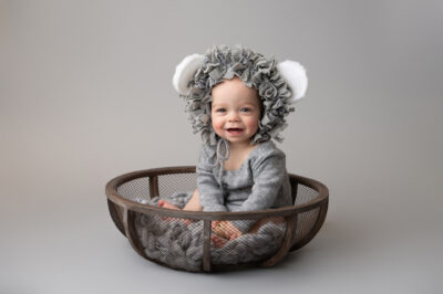 A baby wearing a lion hat sitting in a basket.