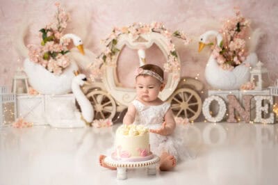A baby girl sitting in front of a cake with swans.