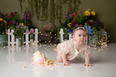 A baby girl crawling on the floor with a cake in front of her.