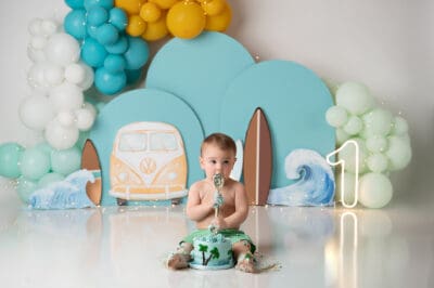 A baby sitting in front of balloons and a vw van.
