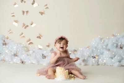 A baby girl is sitting in front of a cake with butterflies in the background.