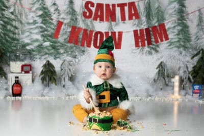 A baby dressed as santa in front of a christmas tree.