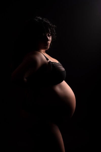 A pregnant woman posing against a dark background.