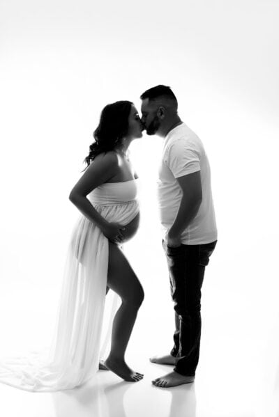 A pregnant couple kissing in front of a white background.
