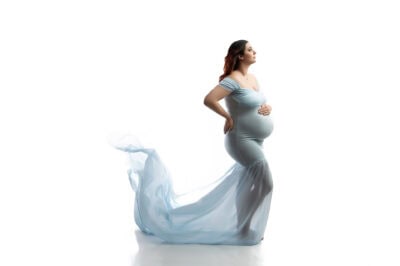A pregnant woman in a blue dress posing on a white background.