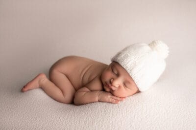 A newborn baby sleeping in a white hat.
