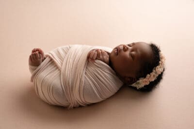 A newborn baby girl wrapped in a blanket on a beige background.