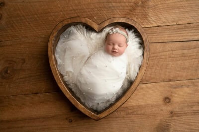 A newborn baby girl is laying in a wooden heart shaped frame.