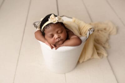A baby girl sleeping in a bucket on a wooden floor.