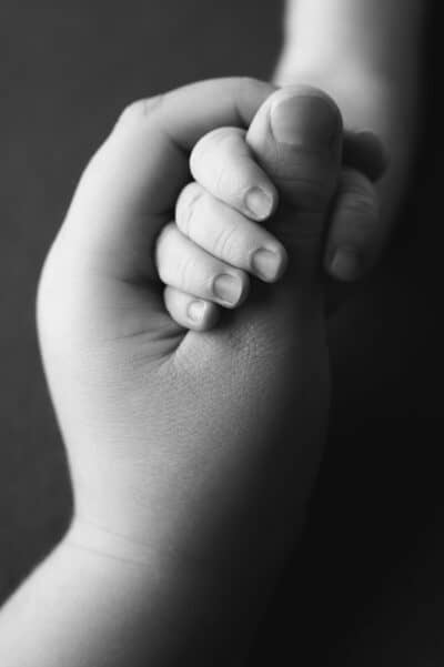 A black and white photo of a hand holding a baby's hand.