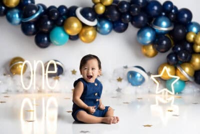 A baby girl sitting in front of balloons for her first birthday.