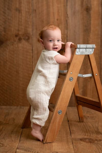 A baby girl is climbing on a wooden ladder.