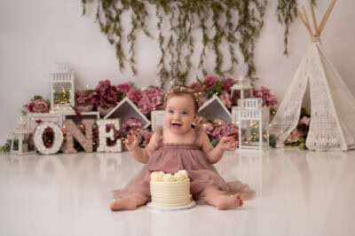 A baby girl with a cake in front of a teepee.