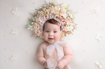 A baby wearing a flower crown in front of a white background.