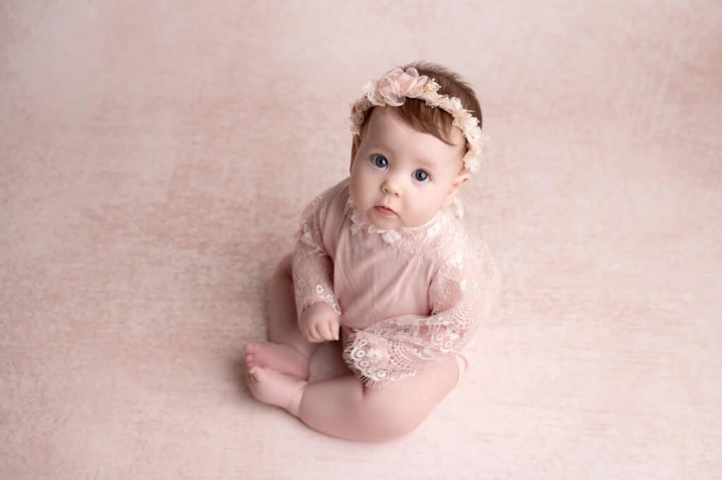 A baby girl sitting on the floor in a pink outfit.