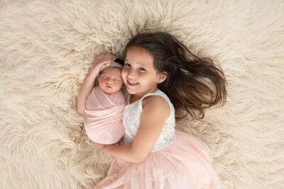 A little girl laying on a fluffy rug with a newborn baby.