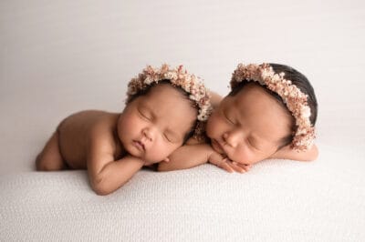 Two newborn twins laying on a white background.