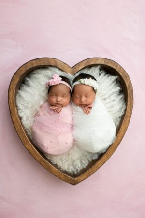 Two newborn twins in a heart shaped wooden box.