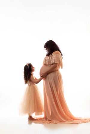 A pregnant woman in a pink dress and a little girl in a pink dress.