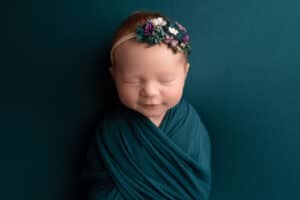A baby girl wrapped in a blue wrap with a flower headband.