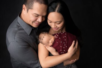 A man and woman are holding their newborn baby on a black background.