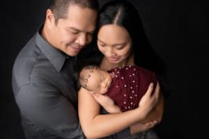 A man and woman are holding their newborn baby on a black background.