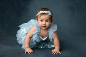 A baby girl in a blue dress crawling on a blue background.