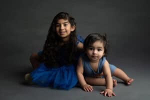 Two children in blue dresses posing on a grey background.