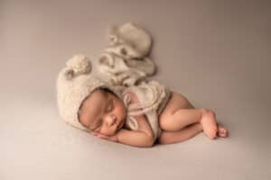 A newborn sleeping in a knitted hat on a gray background.