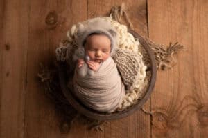 A newborn baby boy wrapped in a blanket on a wooden floor.