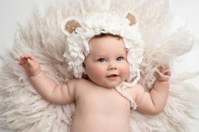 A baby in a white hat laying on a fluffy blanket.
