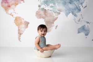 A baby sitting in a bowl in front of a world map.