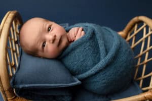 A baby boy wrapped in a blue blanket in a wicker basket.