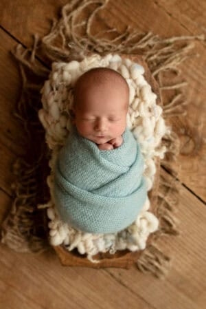 A newborn wrapped in a blue blanket on a wooden table.