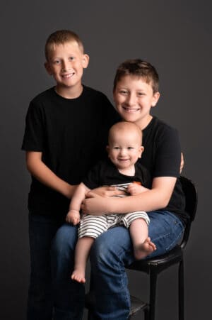 Three boys are posing for a photo in front of a gray background.