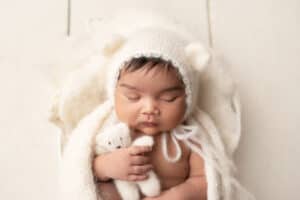 A newborn baby sleeping in a knitted hat with a teddy bear.
