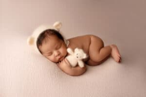 A baby sleeping with a knitted hat and a stuffed animal.