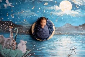 A newborn baby in a blue blanket on a blue background.