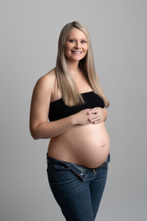 A pregnant woman posing in front of a gray background.