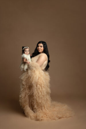 A woman in a white dress holding a baby on a brown background.