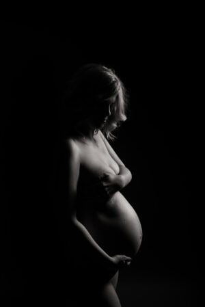 A pregnant woman is posing in front of a black background.