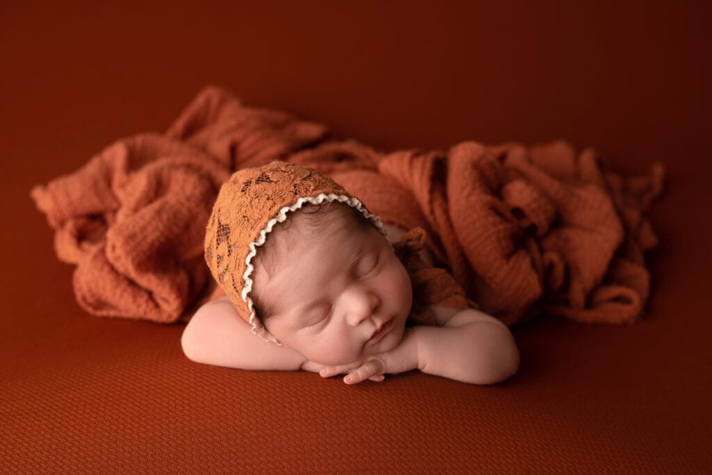 A newborn girl laying on an orange blanket.