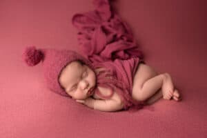 A newborn sleeping on a pink blanket.
