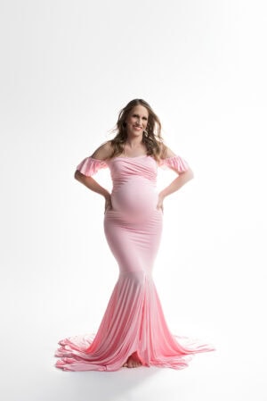 A pregnant woman in a pink dress poses for a photo.