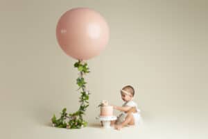 A baby girl sitting in front of a pink balloon.