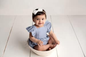 A baby girl in a blue romper sitting in a bowl.