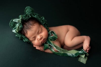 A baby girl in a green hat is laying on a black background.